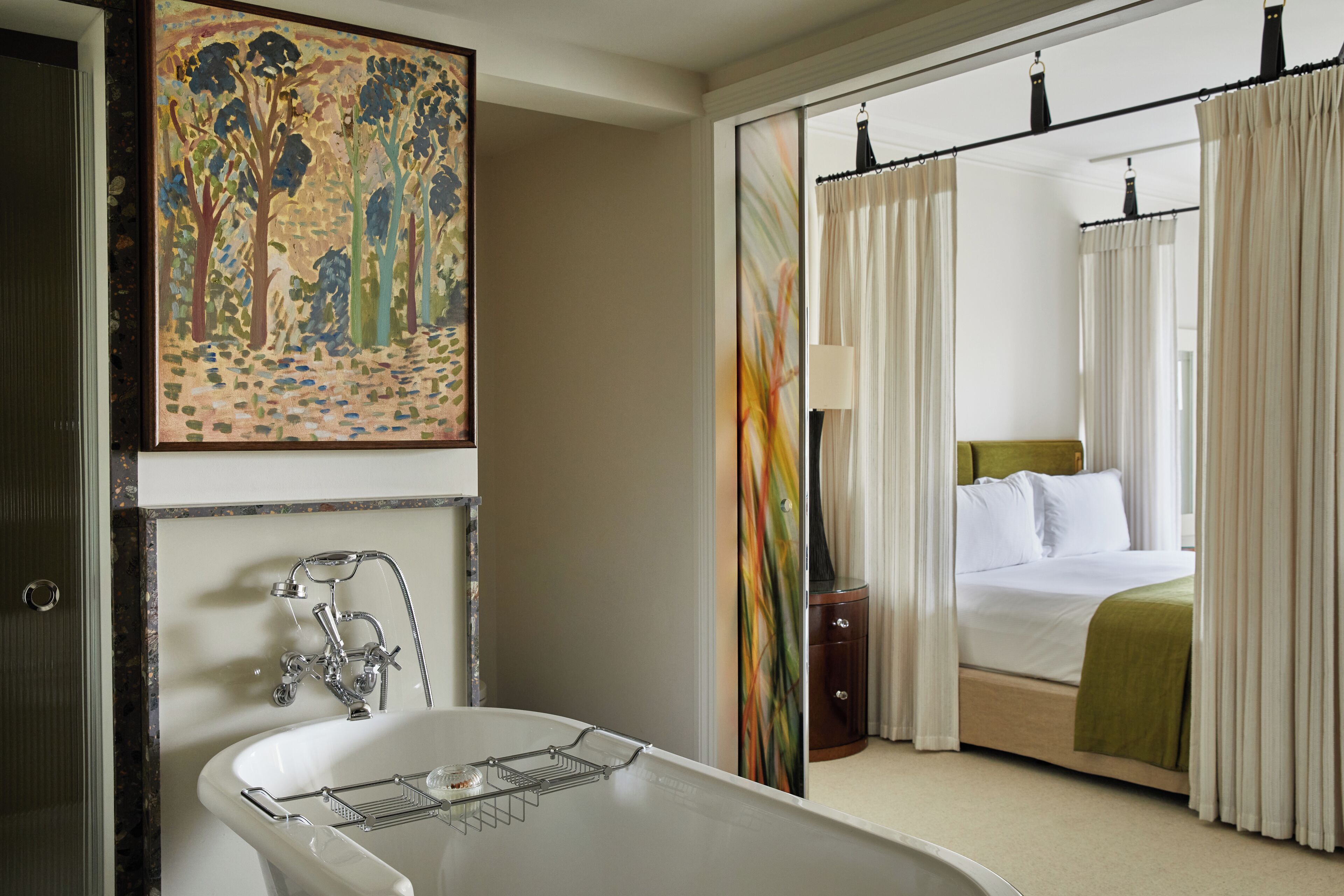Ein Hotelzimmer mit Badewanne, einem Bett mit grüner Decke und einem Baumgemälde an der Wand.