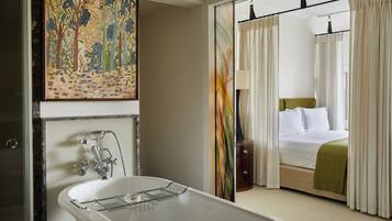 Ein Hotelzimmer mit Badewanne, einem Bett mit grüner Decke und einem Baumgemälde an der Wand.