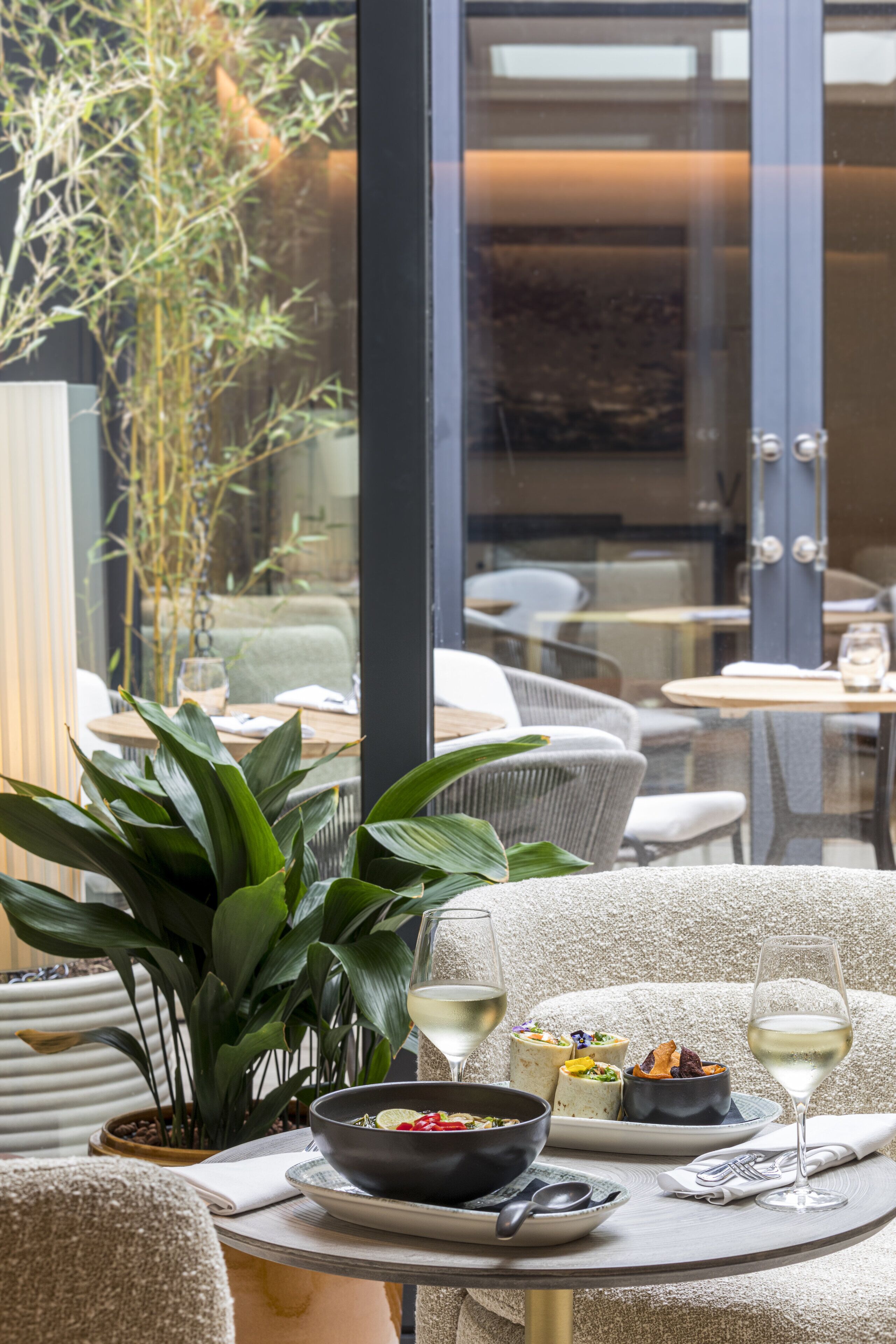 A dining area with a table set for two, featuring a bowl of soup, a plate with a dessert, and two glasses of white wine.