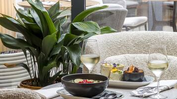 A dining area with a table set for two, featuring a bowl of soup, a plate with a dessert, and two glasses of white wine.