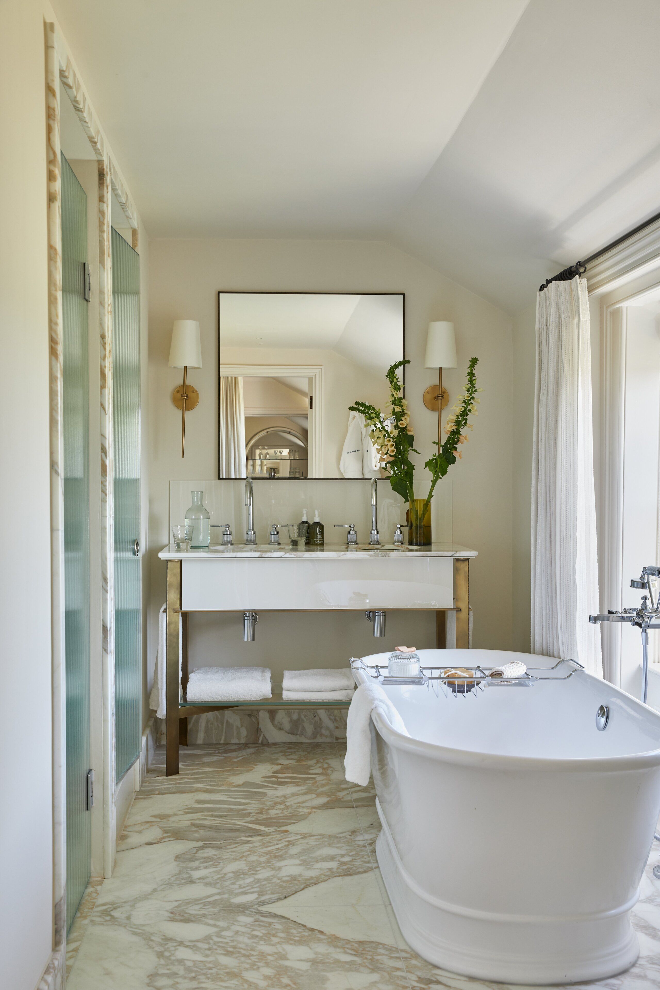 A bathroom with a freestanding bathtub, a vanity with a mirror, and a vase with flowers.
