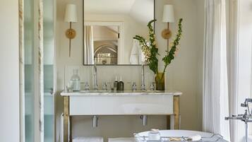 A bathroom with a freestanding bathtub, a vanity with a mirror, and a vase with flowers.