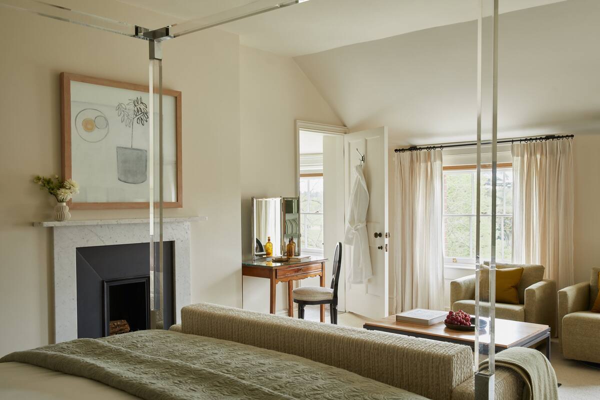 A bedroom with a bed, a desk, a chair, a fireplace, and a window with curtains.