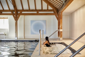 A spa area with a wooden ceiling, a large abstract painting, and a person relaxing in a hot tub.