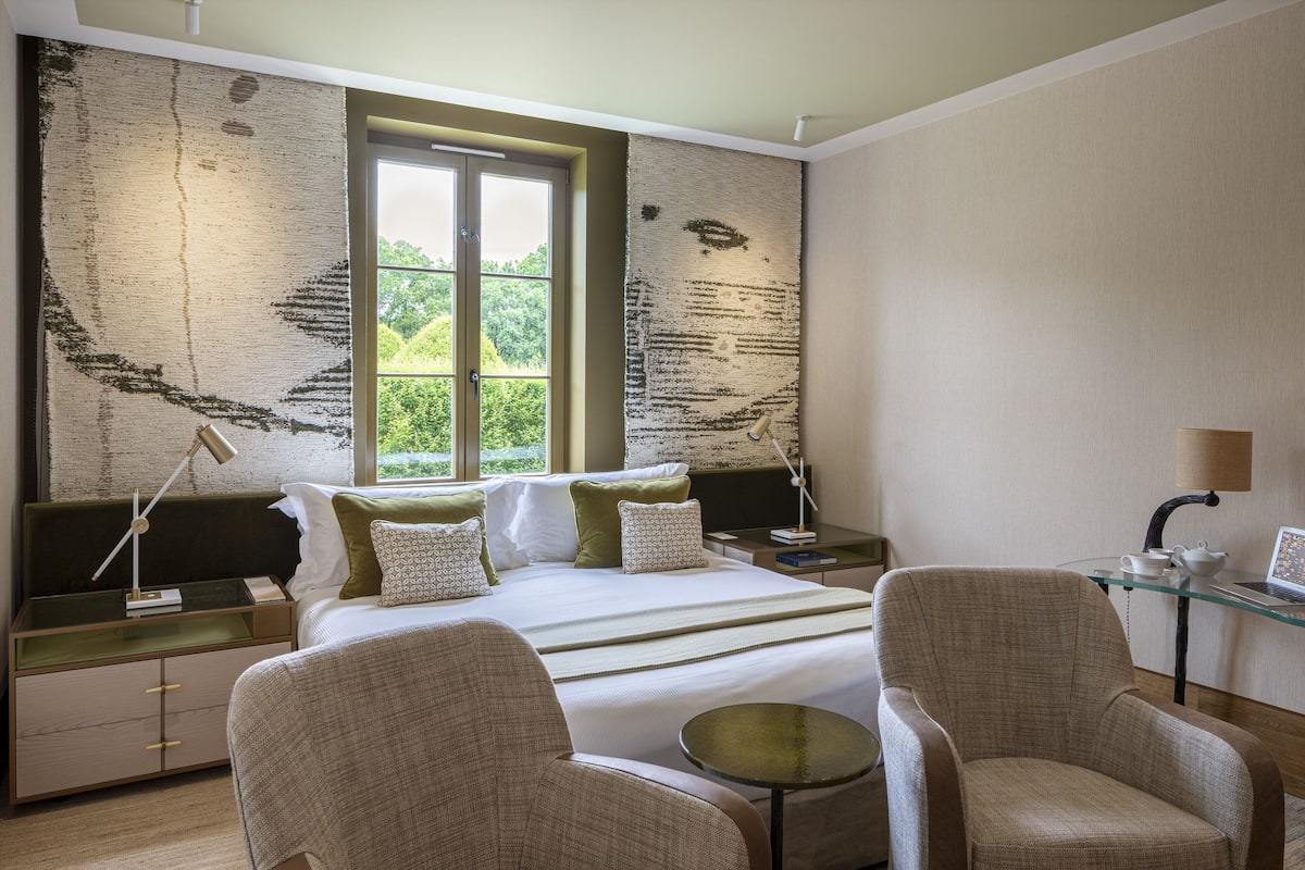 A modern bedroom with a large bed, two bedside tables, a desk, and two armchairs.