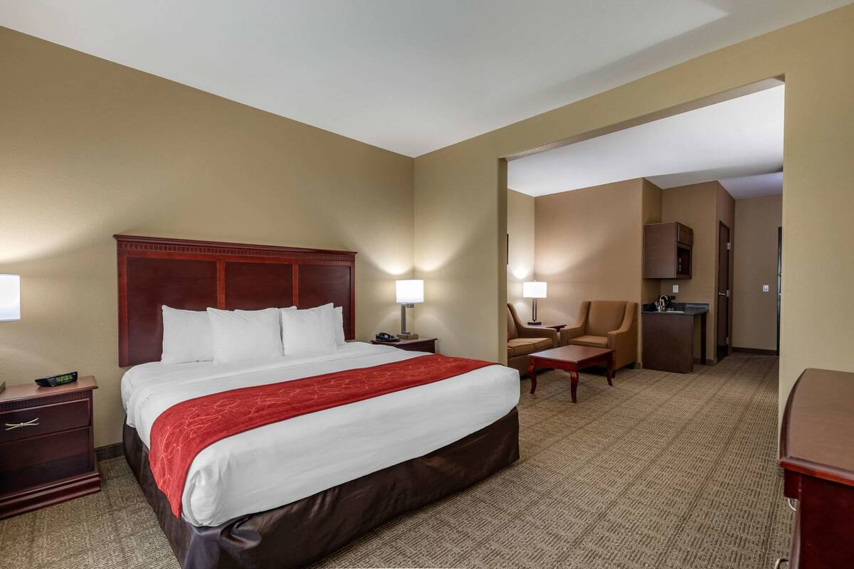 Ein Hotelzimmer mit einem großen Bett, zwei Nachttischen, einem Schreibtisch, einem Stuhl und einer Küchenzeile.