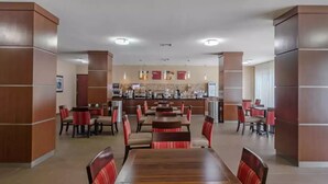Een restaurant met houten tafels en rode stoelen met bekleding, een balie met koffiemachines, en een betegelde vloer.