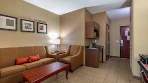 Een hotelkamer met een bank, fauteuil, salontafel en een kitchenette.