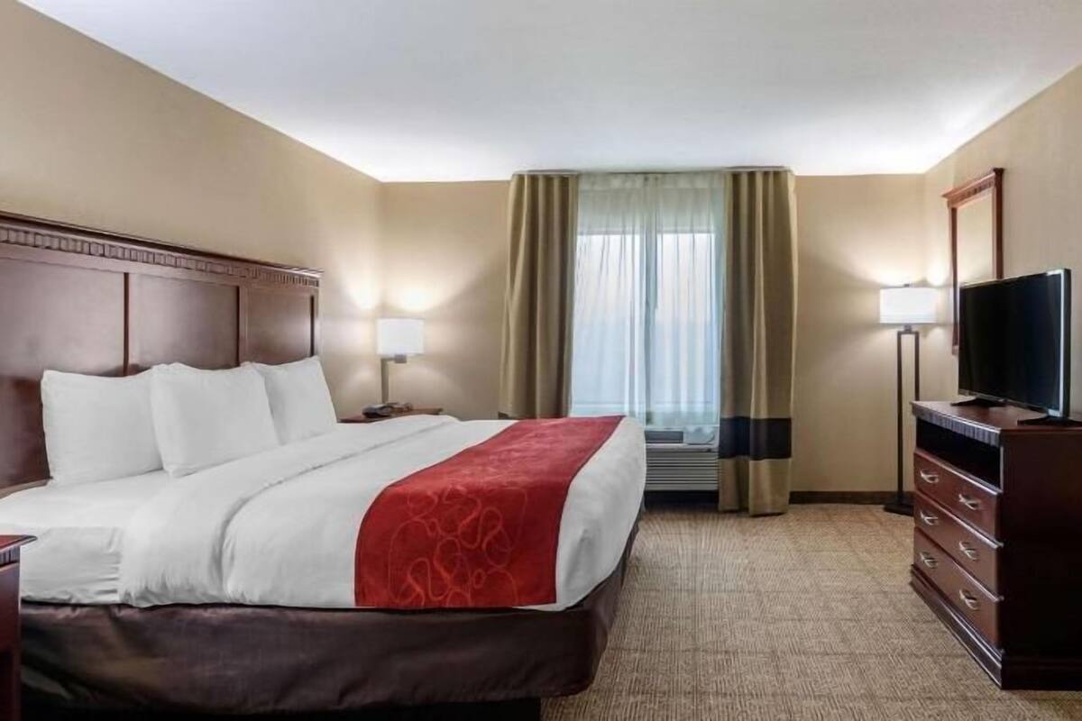 Ein Hotelzimmer mit einem Bett, einem Fernseher, einem Schminktisch und einem Fenster mit Vorhängen.