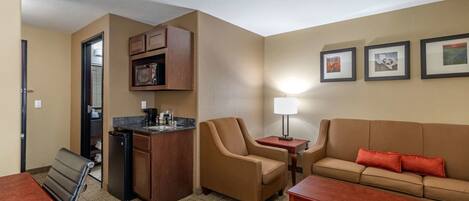 A hotel room with a kitchenette, a sofa, a chair, a dining table, and a lamp.