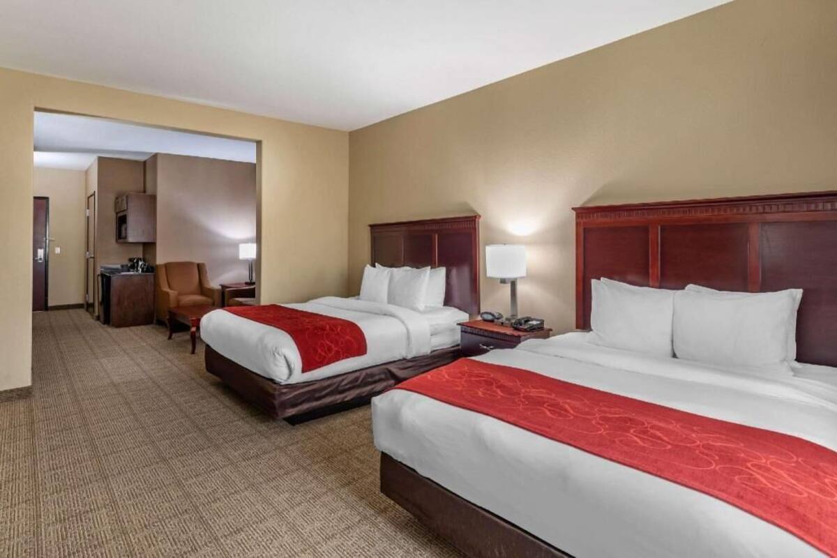 Ein Hotelzimmer mit zwei Betten, einem Sessel, einem Schreibtisch und einer Lampe.