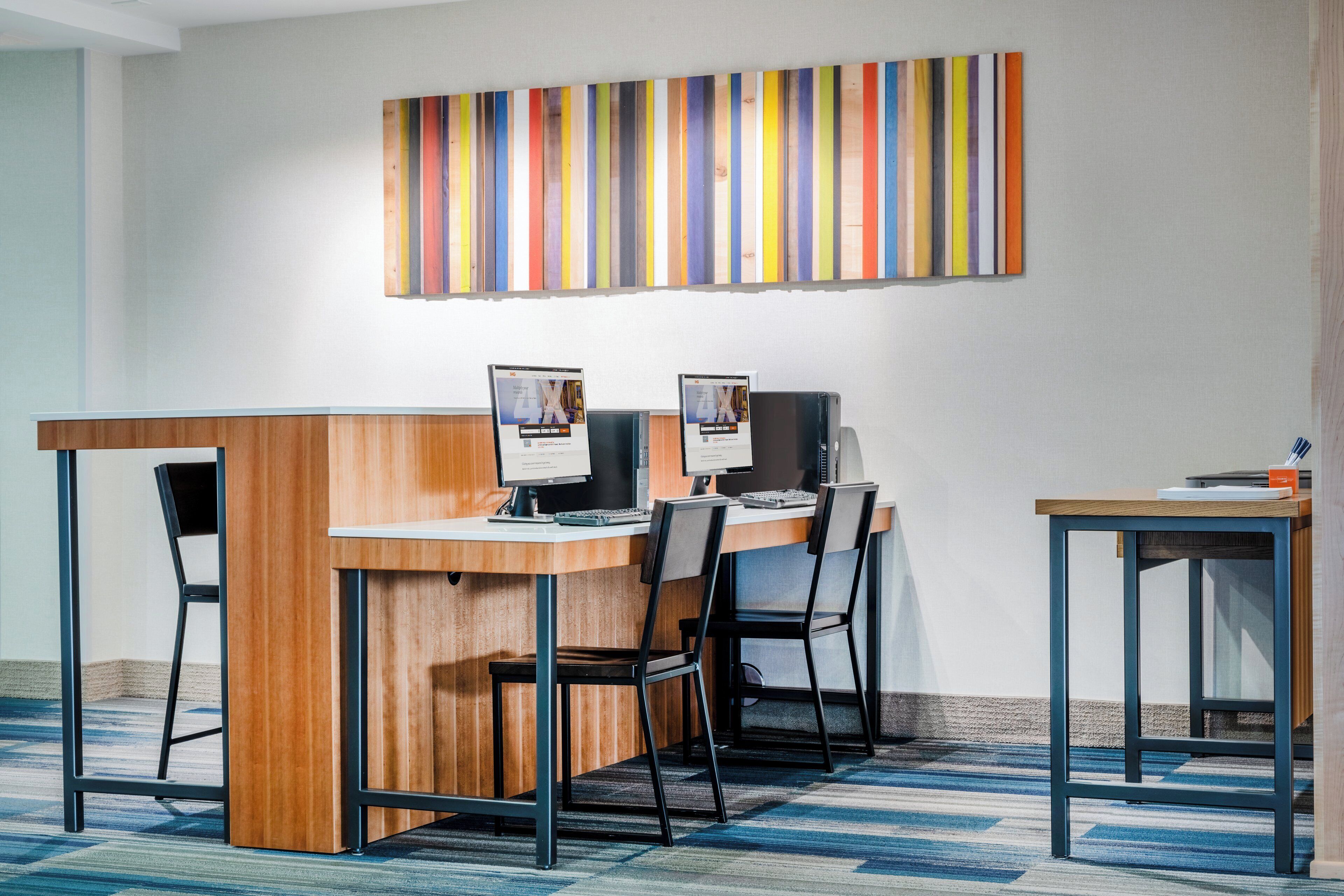A modern office space with a wooden desk, two computer monitors, and a striped artwork on the wall.