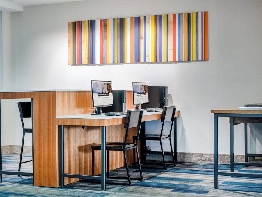 Un espacio de oficina moderno con un escritorio de madera, dos monitores de computadora y una obra de arte a rayas en la pared.