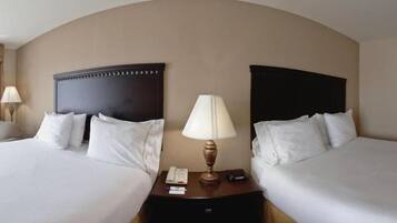 A hotel room with two beds, each with a dark headboard, a bedside table with a lamp, and a telephone.