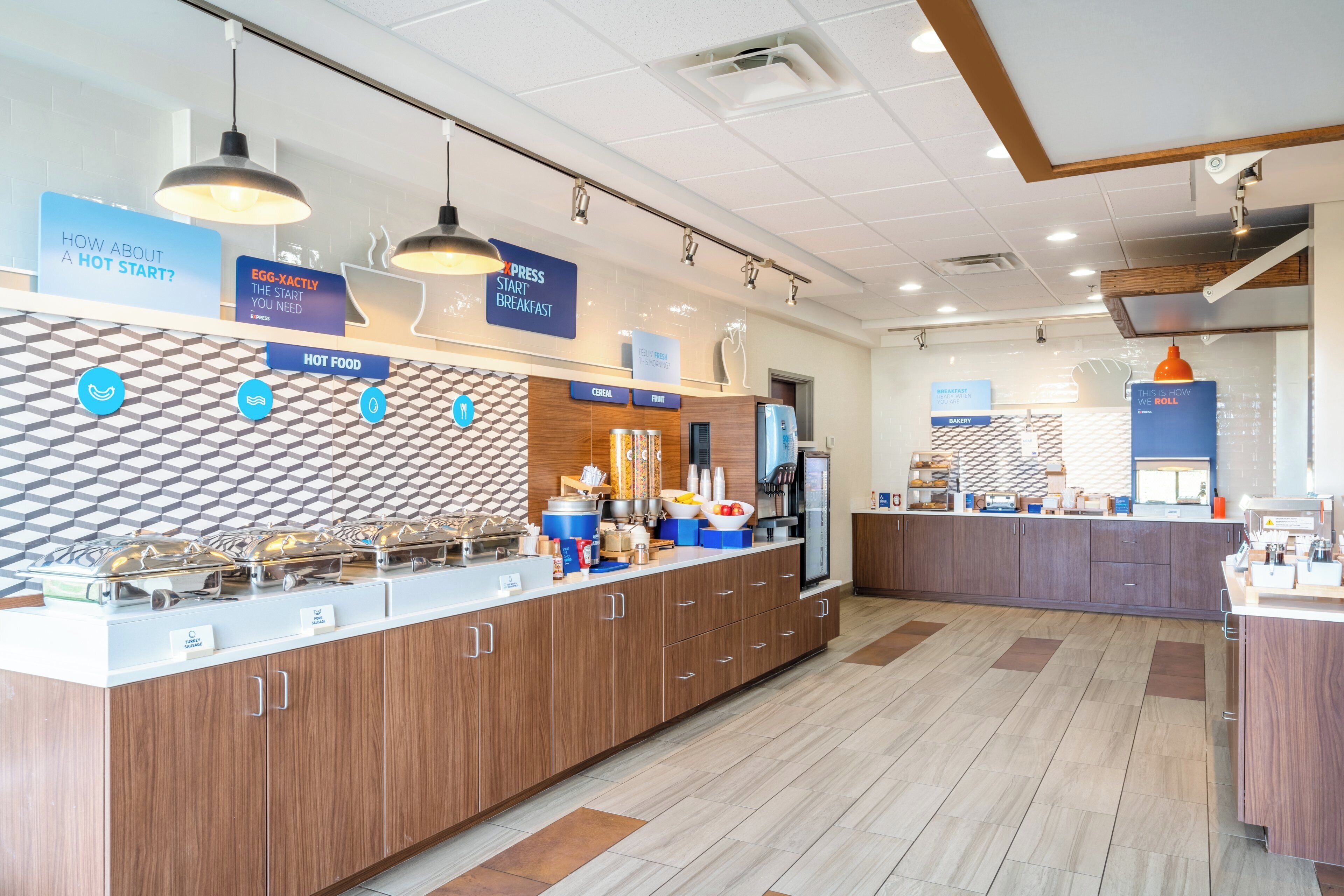 A breakfast area with a counter displaying hot food options, a refrigerator, and a coffee machine.
