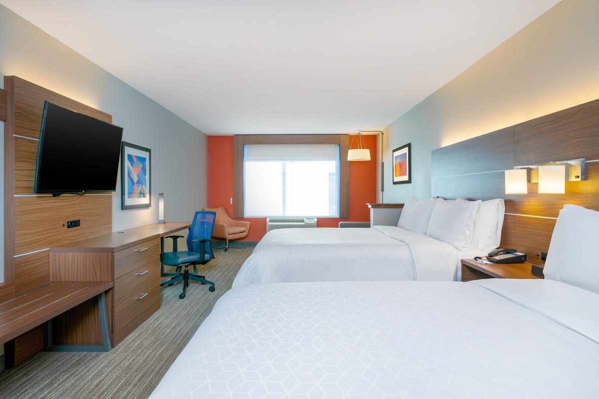 A hotel room with two beds, a desk, a chair, a TV, and a window with a view.