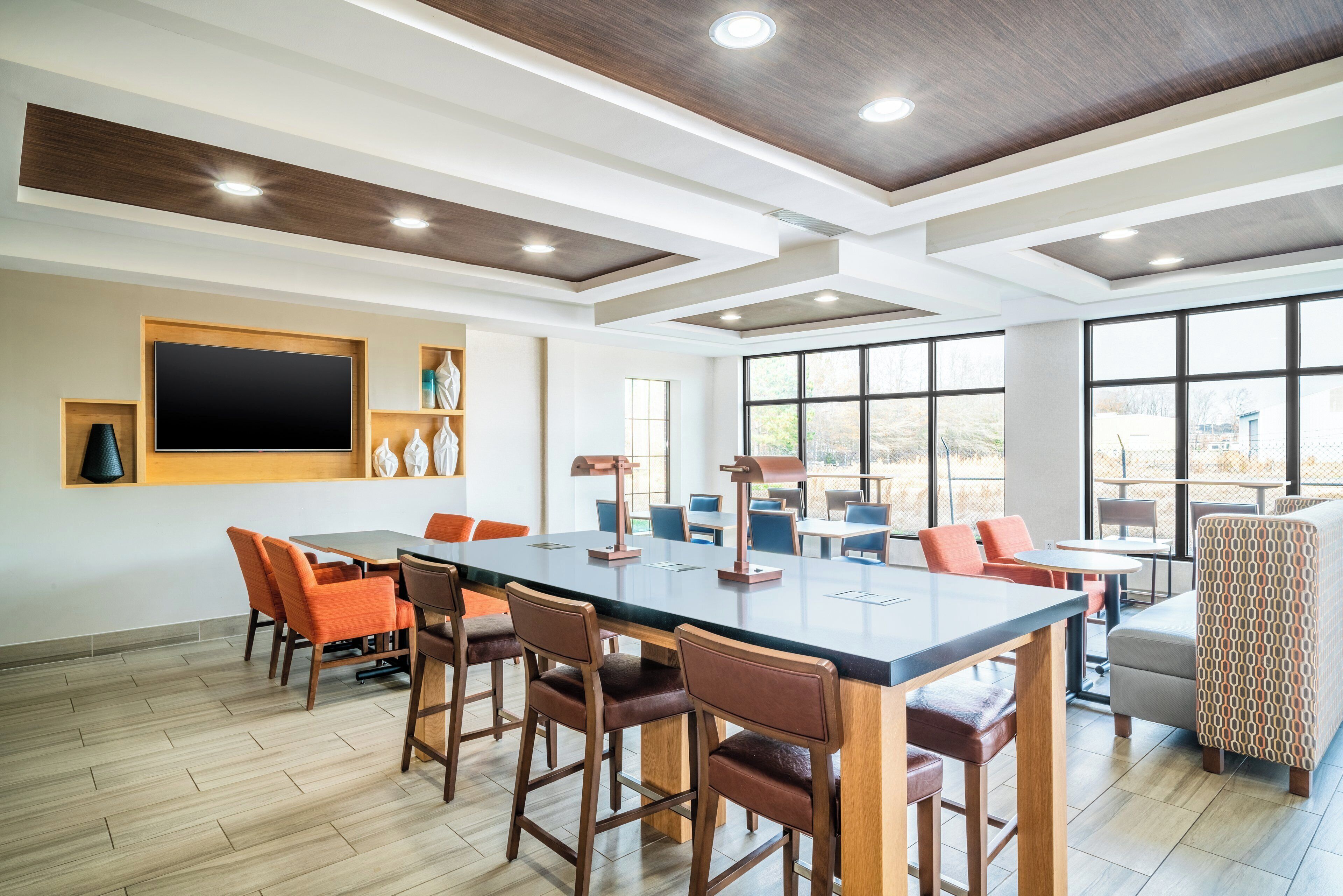 A spacious room with a large table and chairs, a flat-screen TV mounted on the wall, and large windows offering a view of the outdoors.