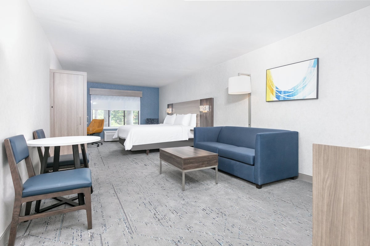 A hotel room with a bed, a blue sofa, a wooden coffee table, and a white round table with chairs.