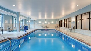 Ein Hallenbad mit deutlicher Beschilderung, einem Rettungsschwimmerstuhl und einer Wanduhr.