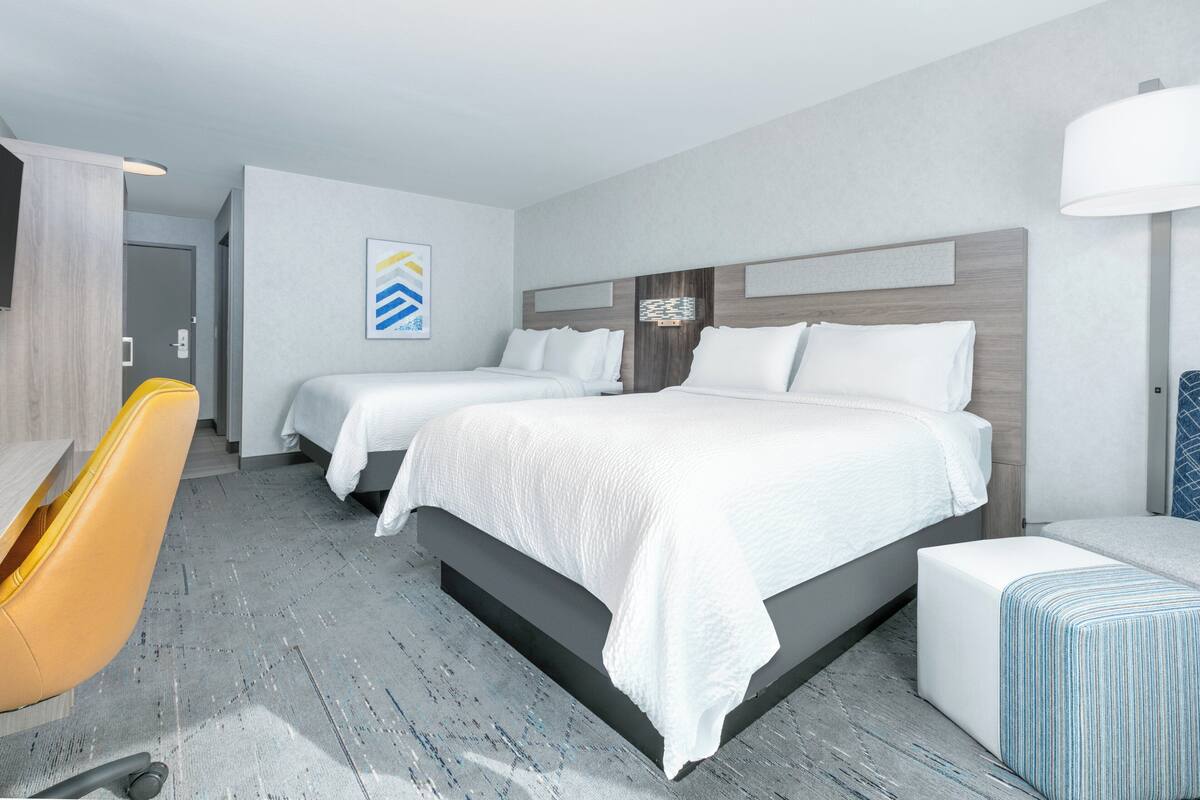 A hotel room with two beds, a desk, and a chair.