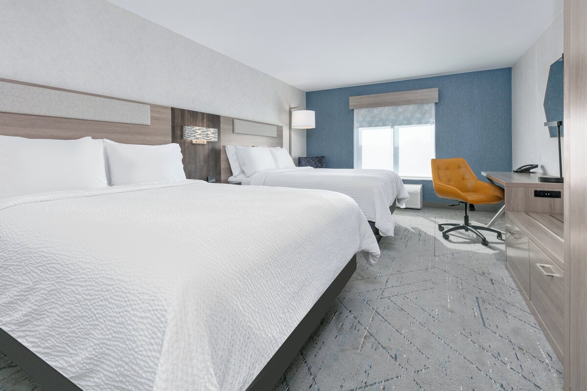 A hotel room with two beds, a desk, a chair, and a window.
