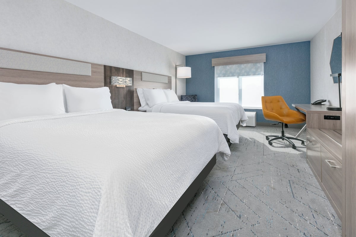 A hotel room with two beds, a desk, a chair, and a window.