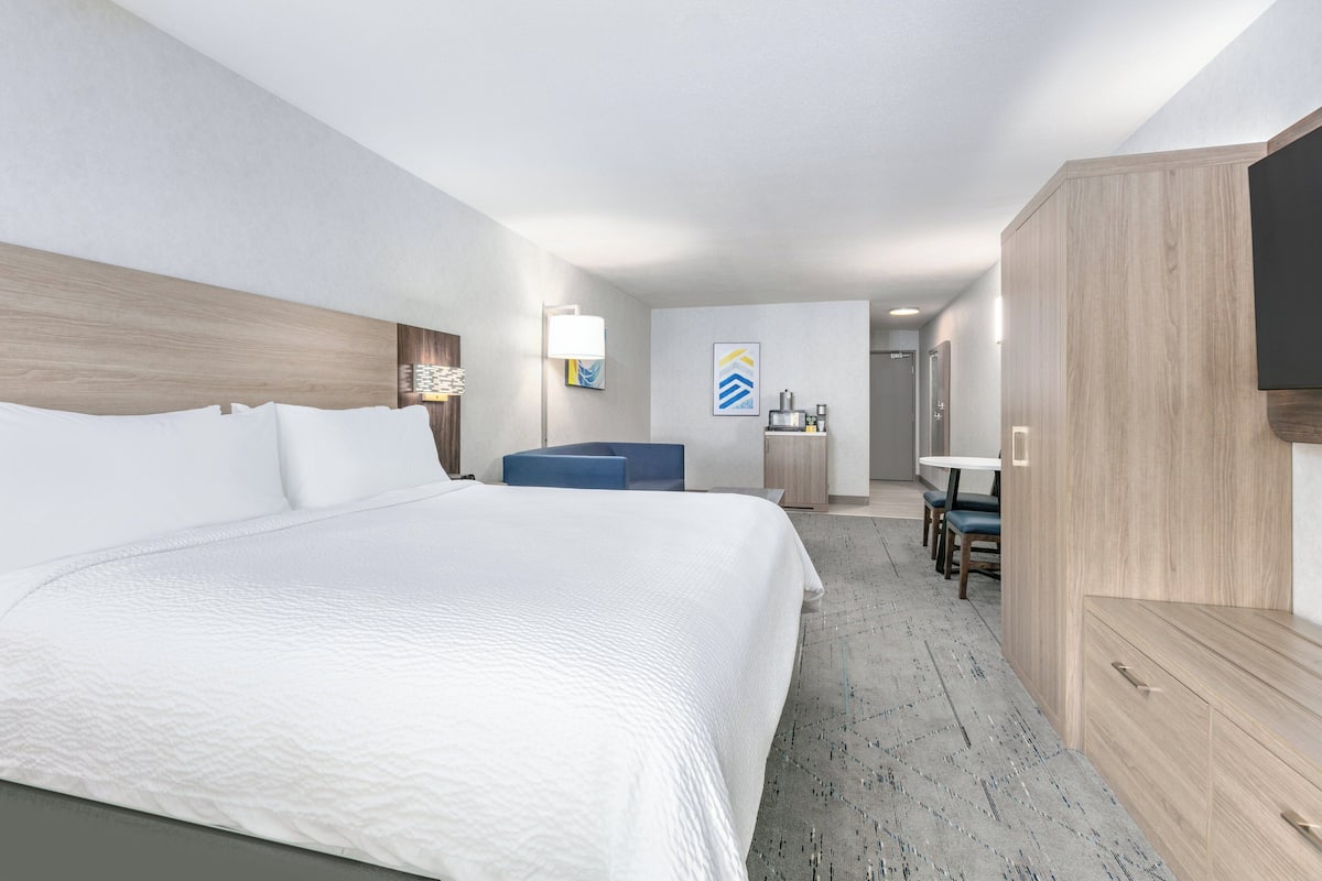 A hotel room with a large bed, a desk, a chair, and a television.