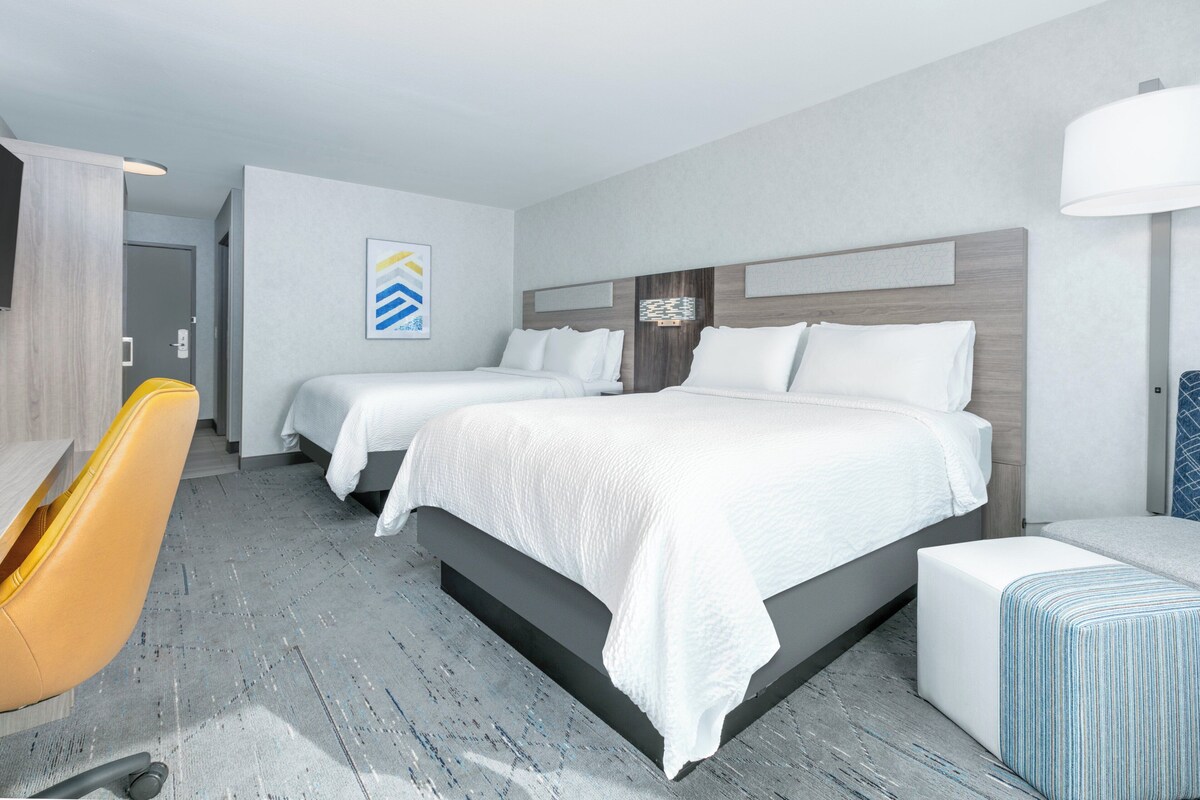 A hotel room with two beds, a desk, and a chair.