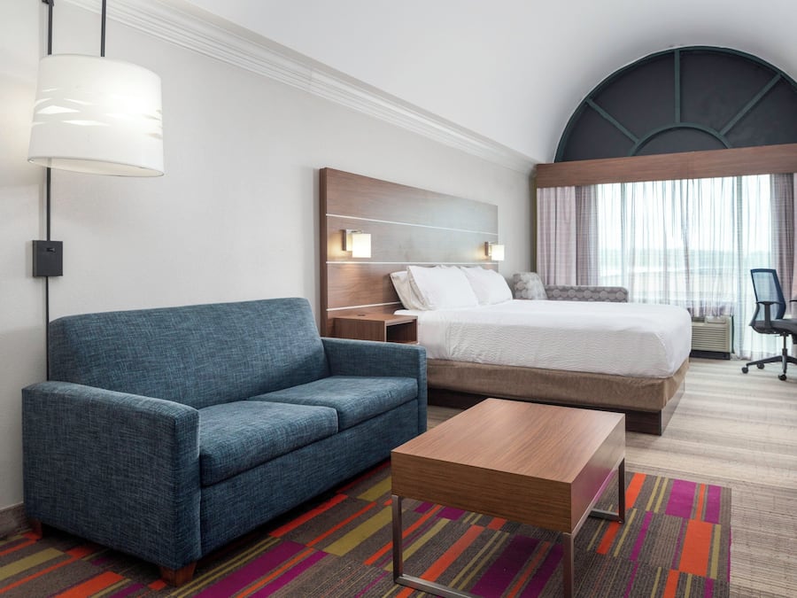 A hotel room with a bed, a sofa, a desk, a chair, and a lamp.