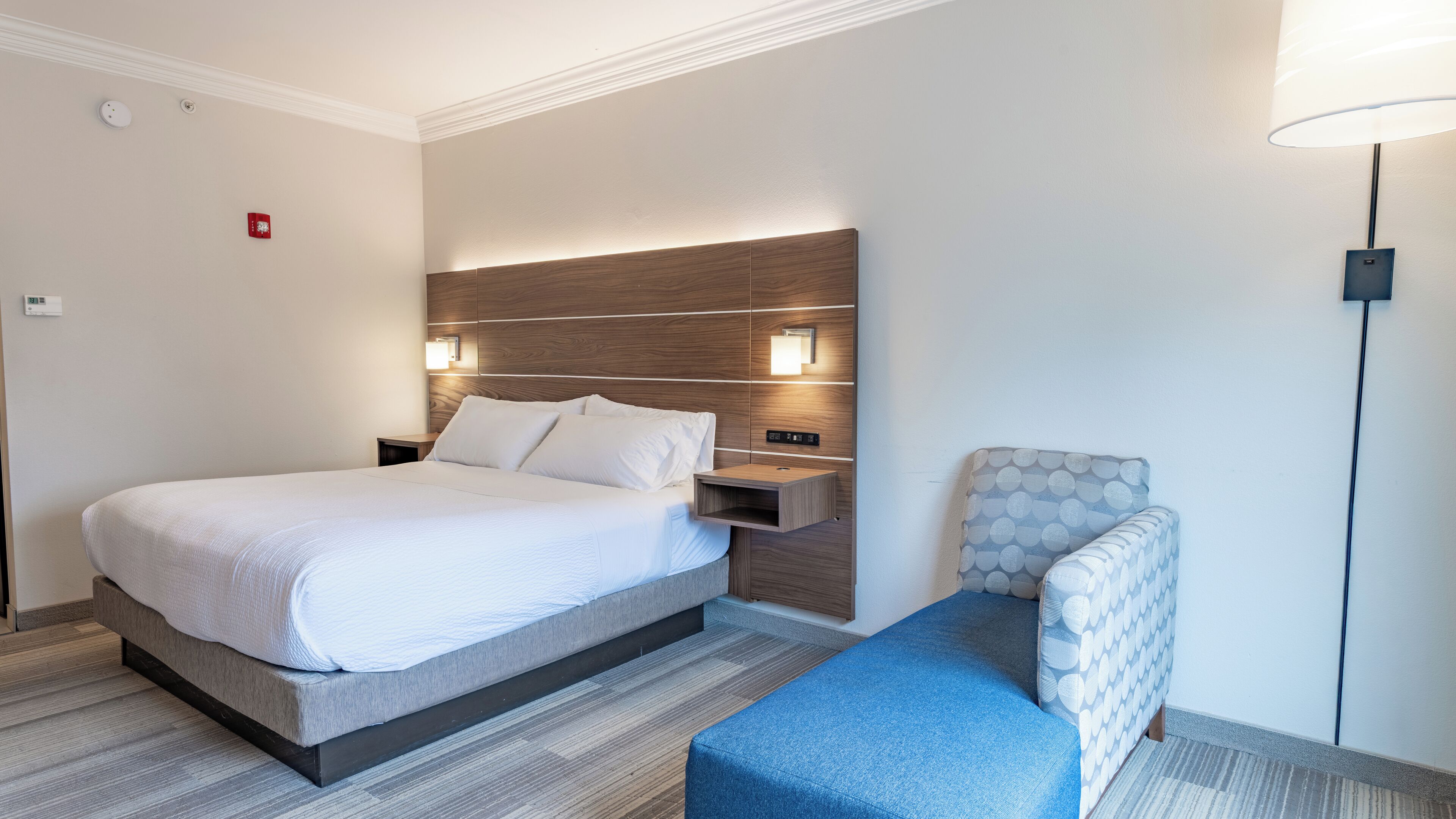 Een moderne hotelkamer met een groot bed, nachtkastjes, een fauteuil en een lamp.