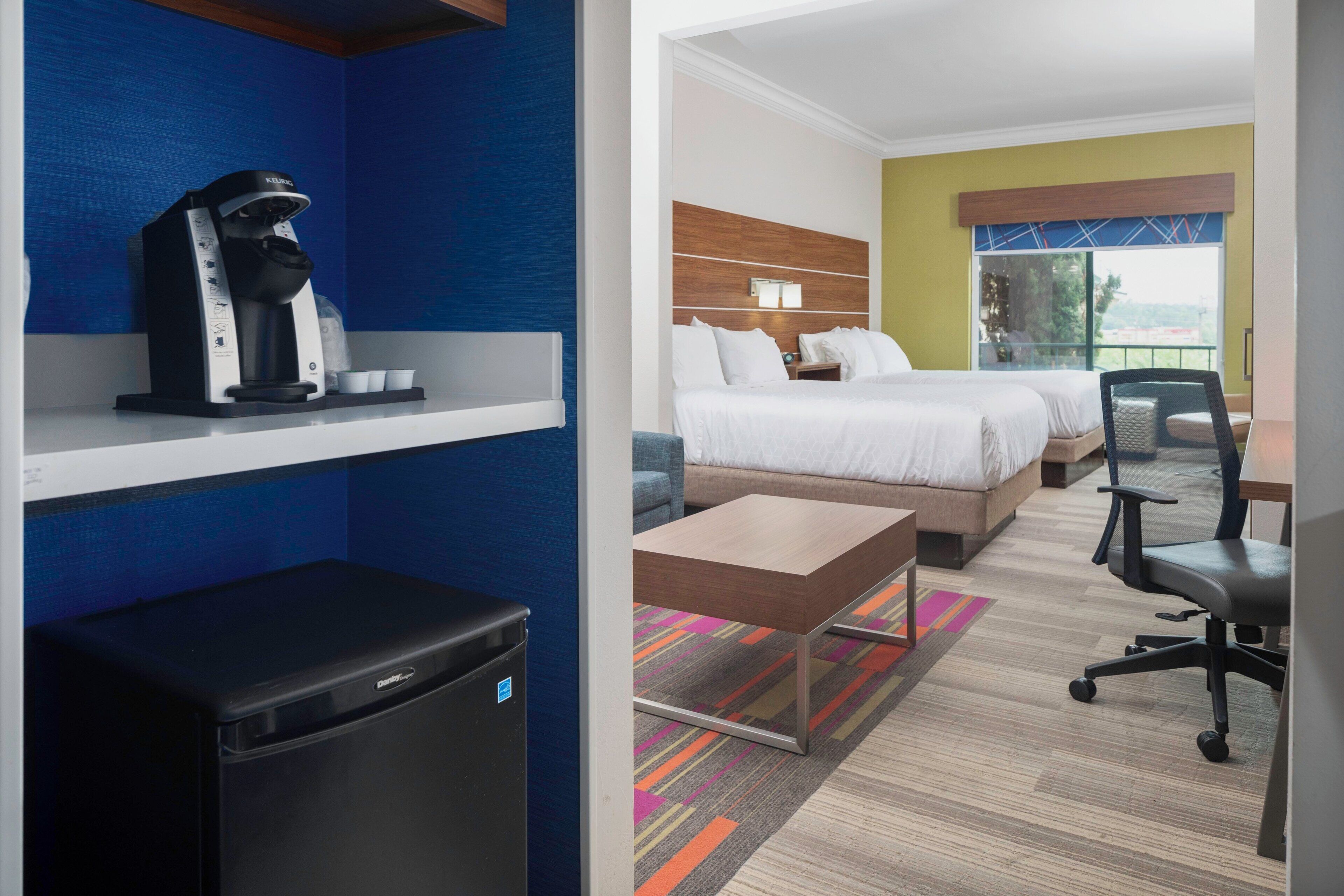 A hotel room with a bed, a desk, a chair, a coffee maker, and a television.