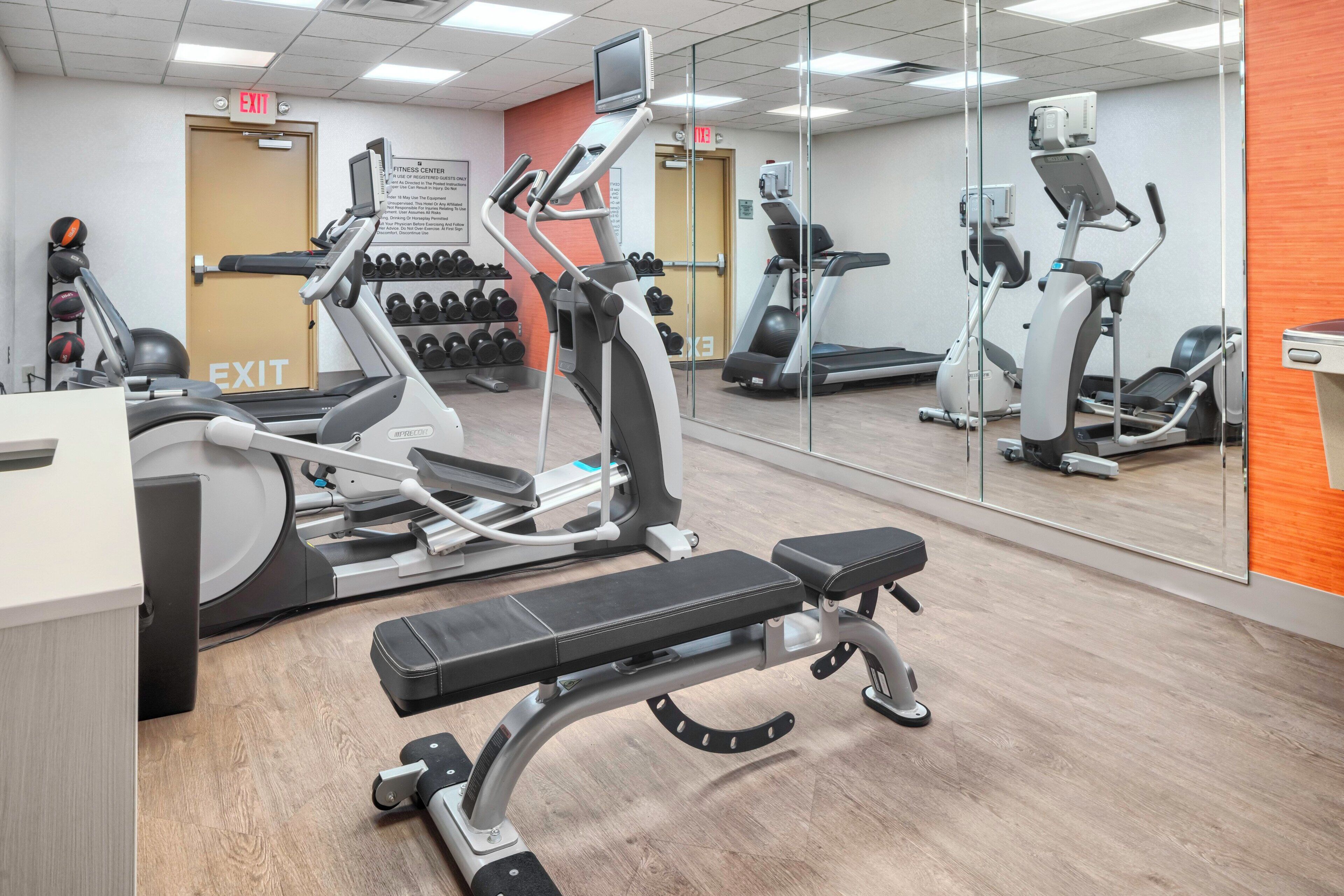 Academia com equipamentos de exercício, um banco e um espelho grande.