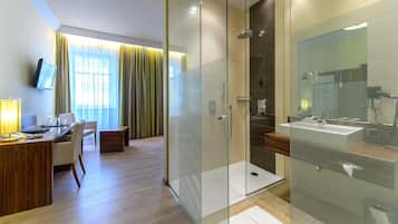 Ein modernes Hotelzimmer mit einer gläsernen Dusche, einem Holztisch mit Stuhl und einem großen Fenster mit Vorhängen.