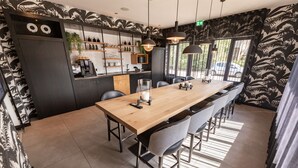 A modern bar area with a long wooden table, black and white patterned walls, and a view of the outside through large windows. - Gr8 Hotel Sevenum (Sevenum)