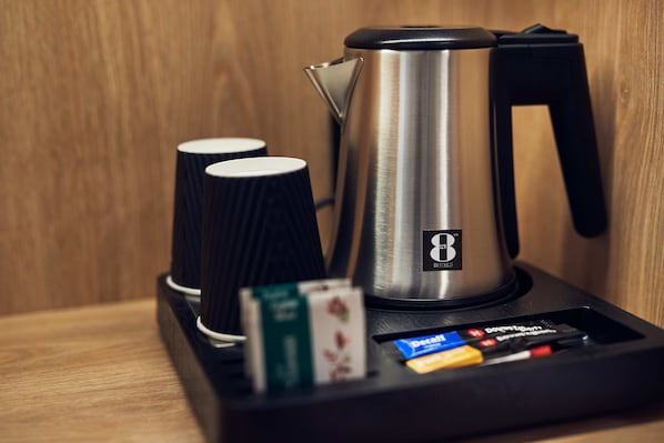 Una cafetera con dos tazas y una caja de té sobre una superficie de madera.