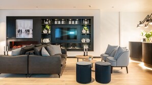 A modern living room with a sofa, armchairs, ottomans, a TV, and a fireplace. - Gr8 Hotel Sevenum (Sevenum)