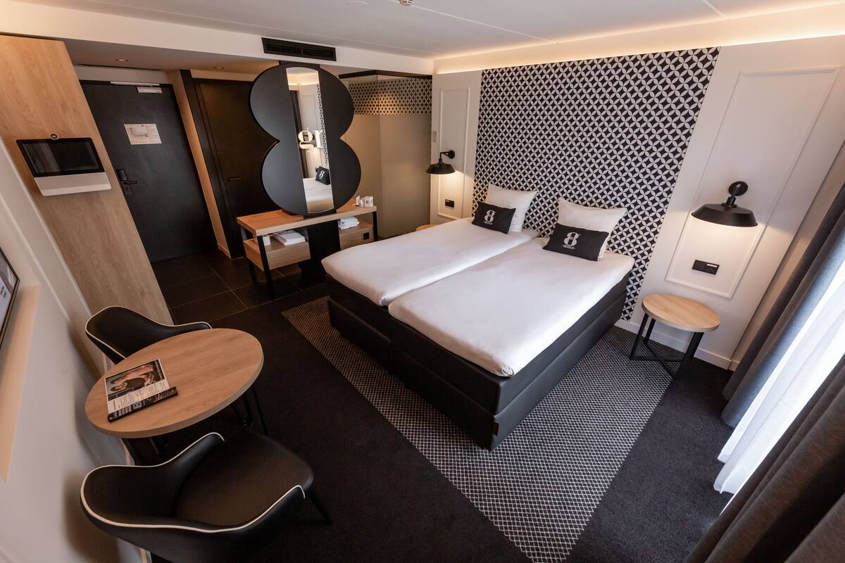 Une chambre d’hôtel moderne équipée d’un lit double, d’un bureau avec une chaise, d’une petite table ronde et d’un miroir.