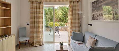 Una sala de estar con un sofá, una silla, una mesita con una planta y vistas a un jardín a través de una puerta corrediza de vidrio.