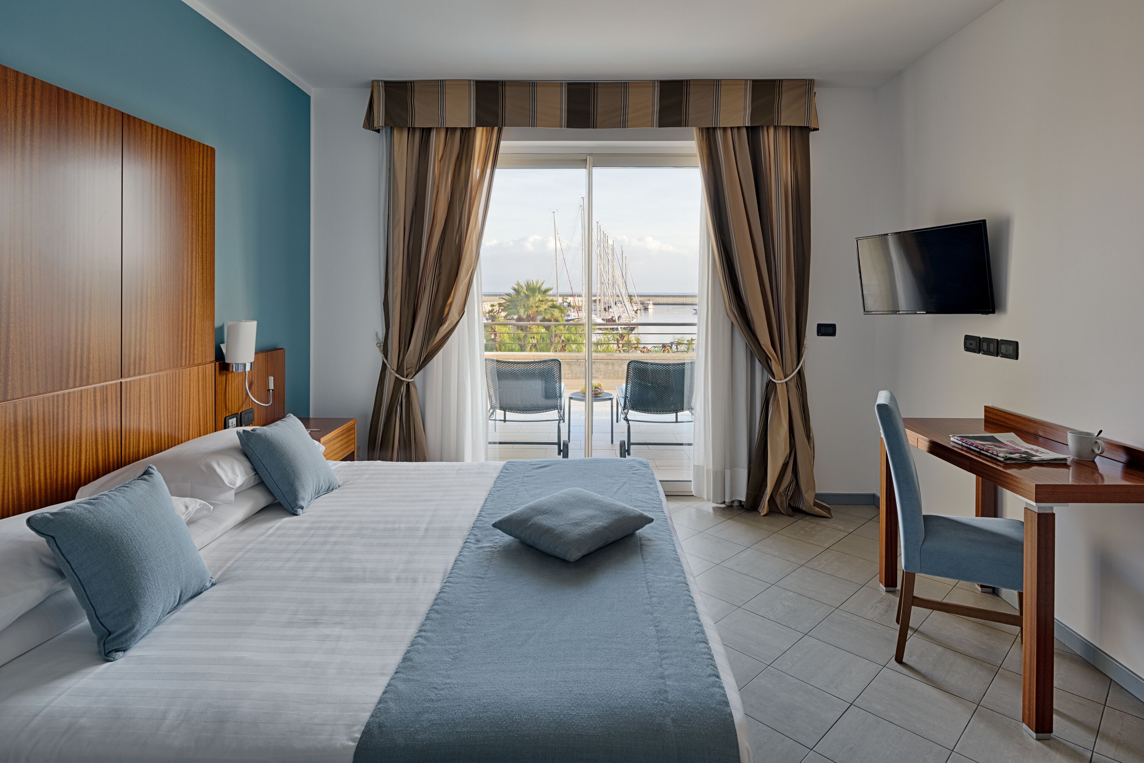 Ein Hotelzimmer mit Bett, Schreibtisch, Fernseher und einem Balkon mit Meerblick.