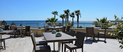 An outdoor patio with tables and chairs, overlooking a clear blue sky and the sea.