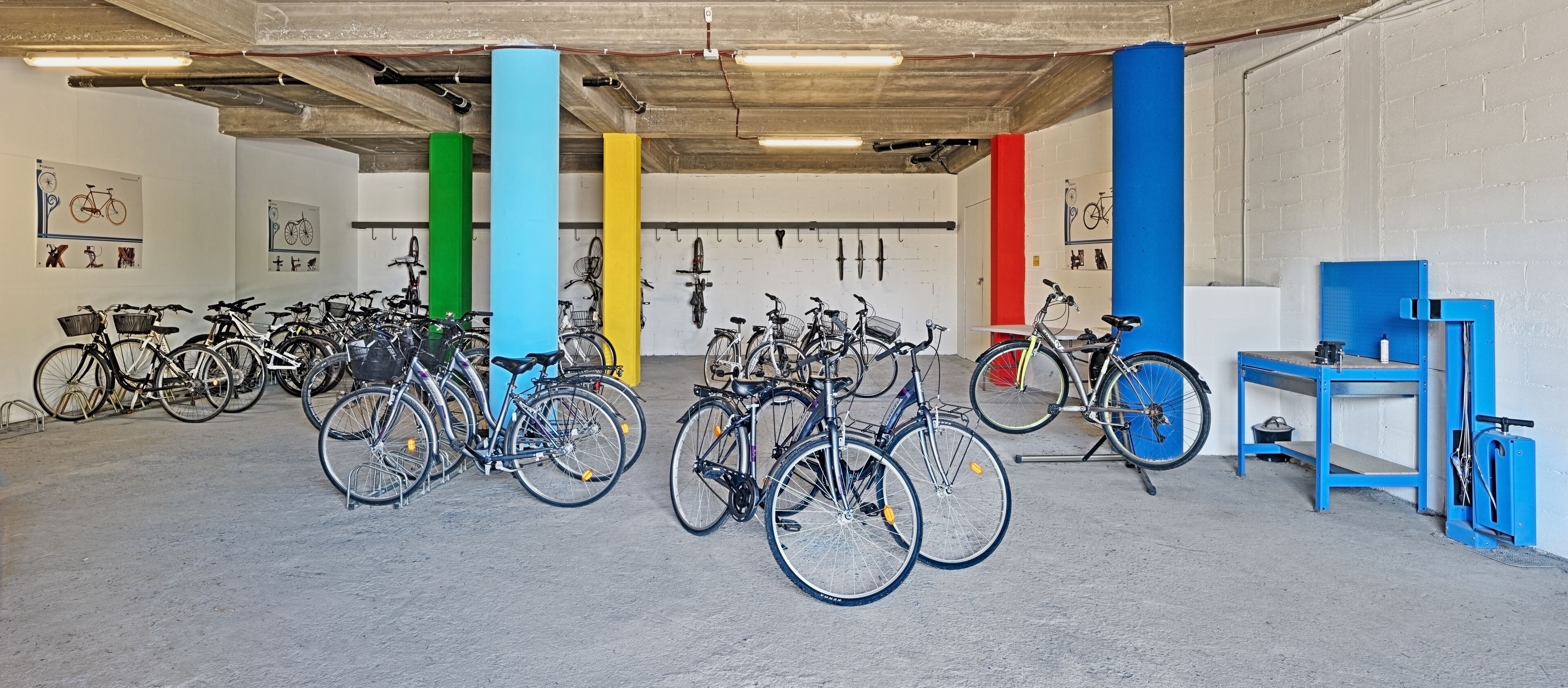 A bicycle storage area with multiple bikes, colorful vertical supports, and a blue table with tools.
