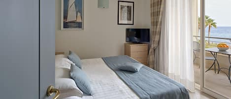 A hotel room with a bed, a TV, and a balcony with a view of the sea.