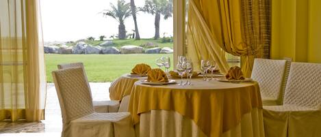 A dining area with a table set for four, overlooking a grassy landscape with palm trees.