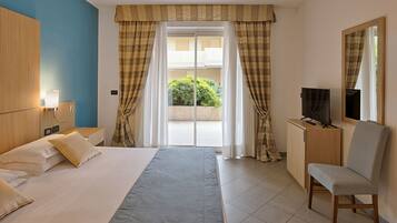 A hotel room with a bed, a desk with a TV, a chair, and a window with curtains.