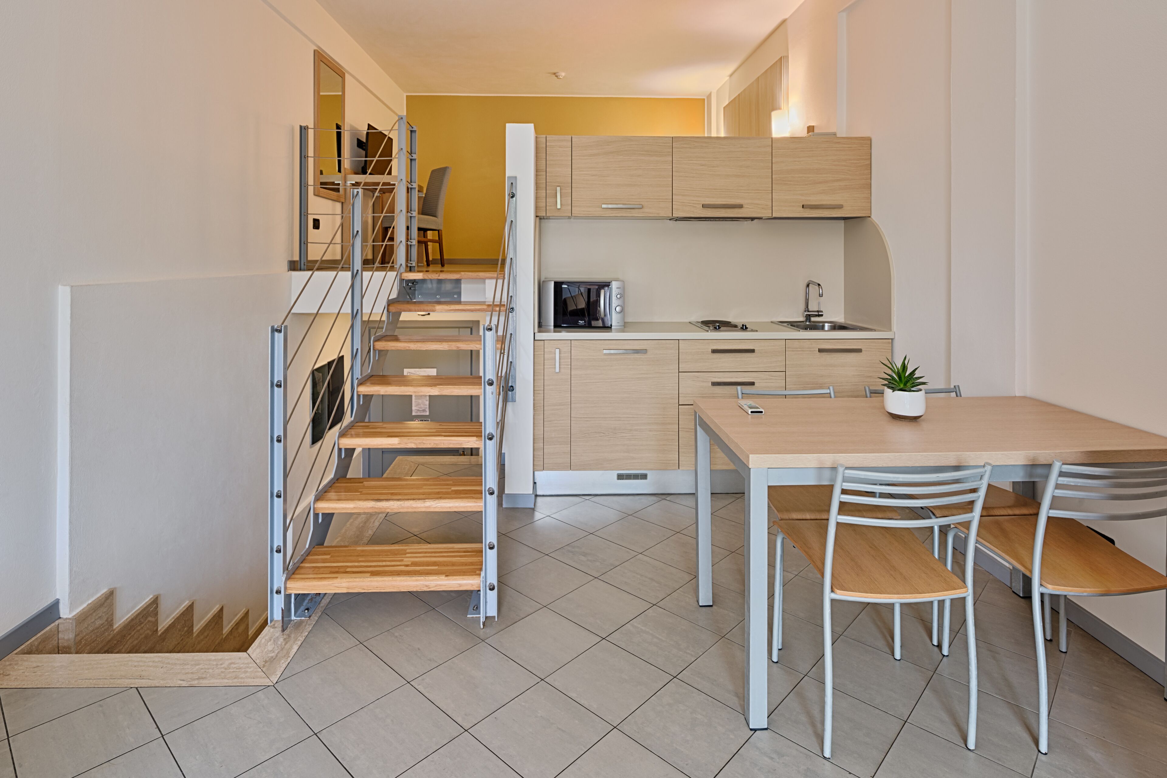 A modern kitchen with a dining area, wooden staircase, and a view of the living area.