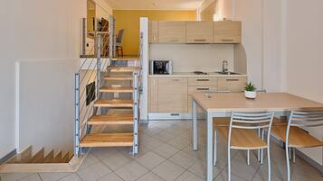 A modern kitchen with a dining area, wooden staircase, and a view of the living area.