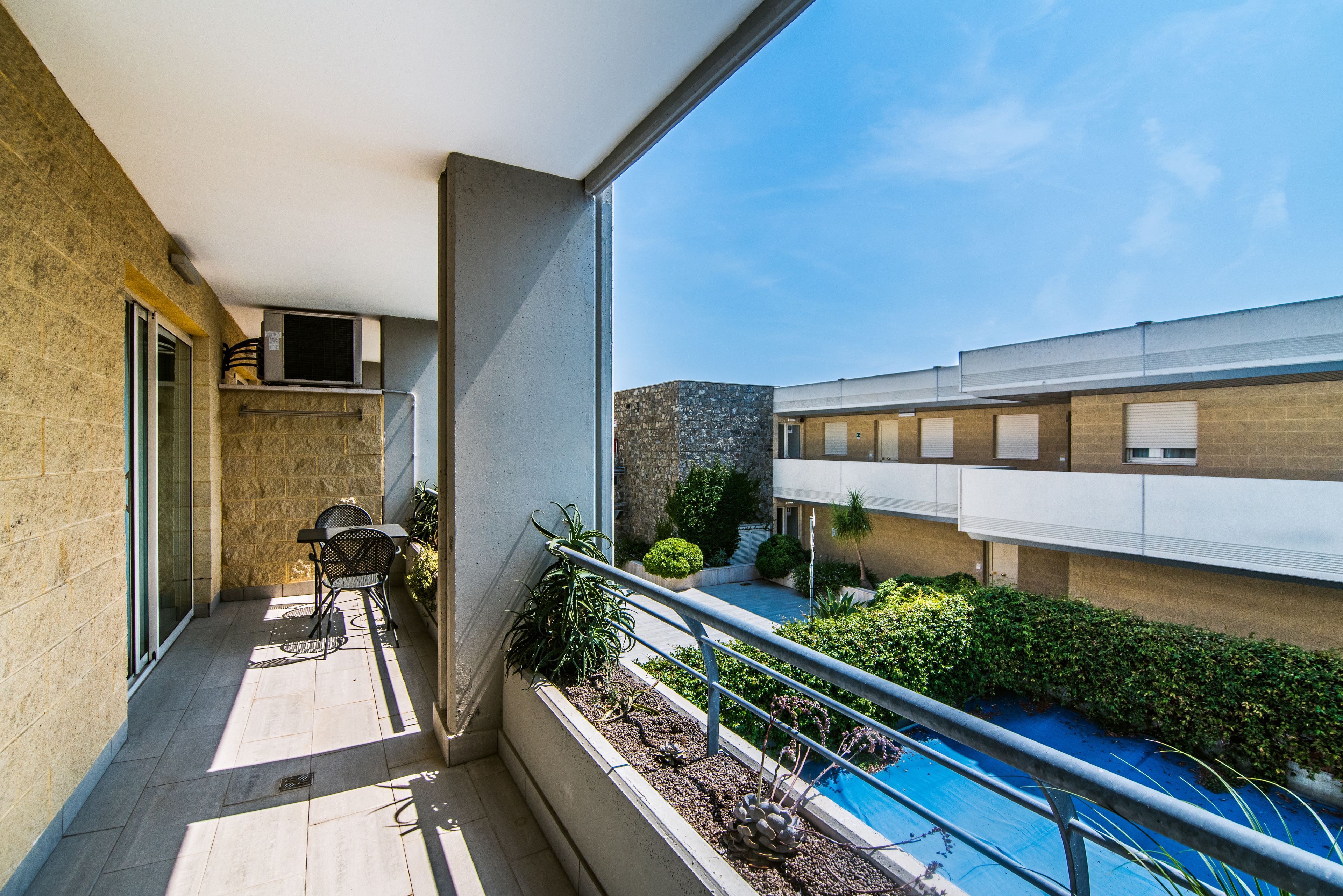 Un balcon avec une piscine, un espace salon extérieur et une vue sur un immeuble à la façade en pierre.