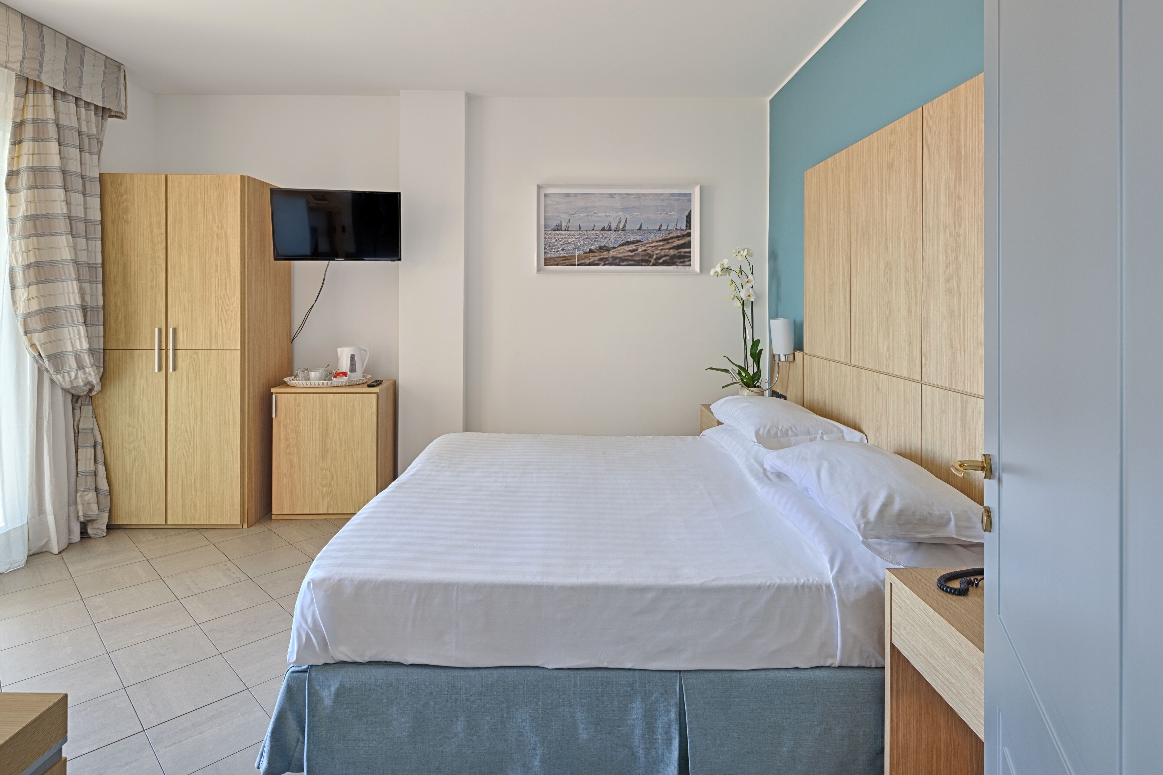 Un dormitorio ordenado con cama, mesita de noche, televisor montado en la pared y armario.