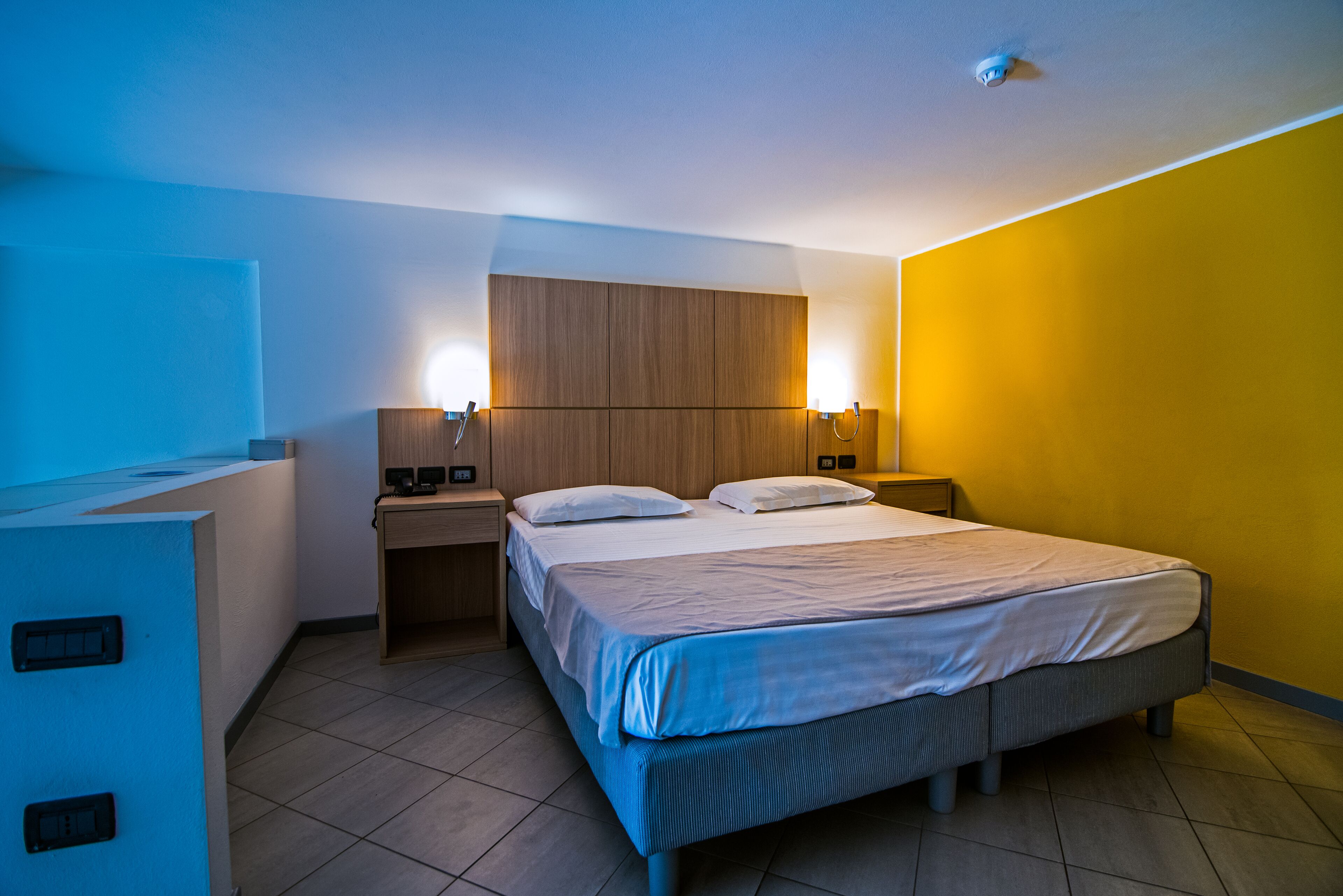 A hotel room with a bed, bedside tables, and a wardrobe.
