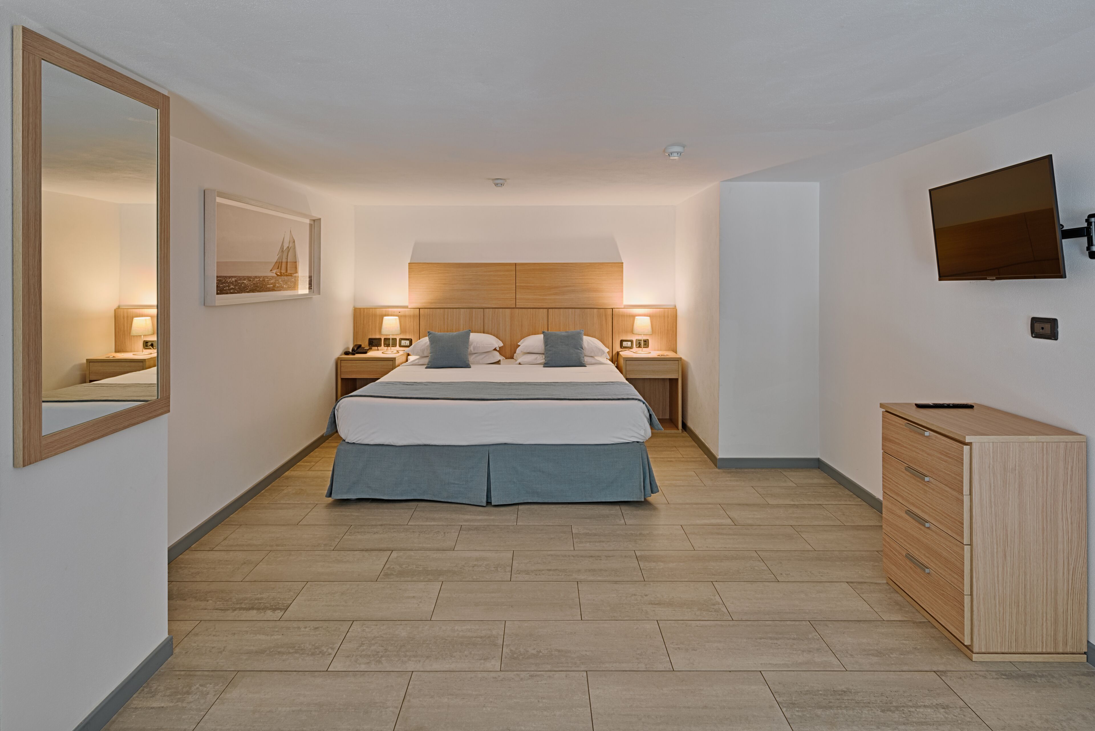 Une chambre à coucher moderne, avec un lit, des tables de chevet, une commode, un téléviseur et un tableau encadré au mur.